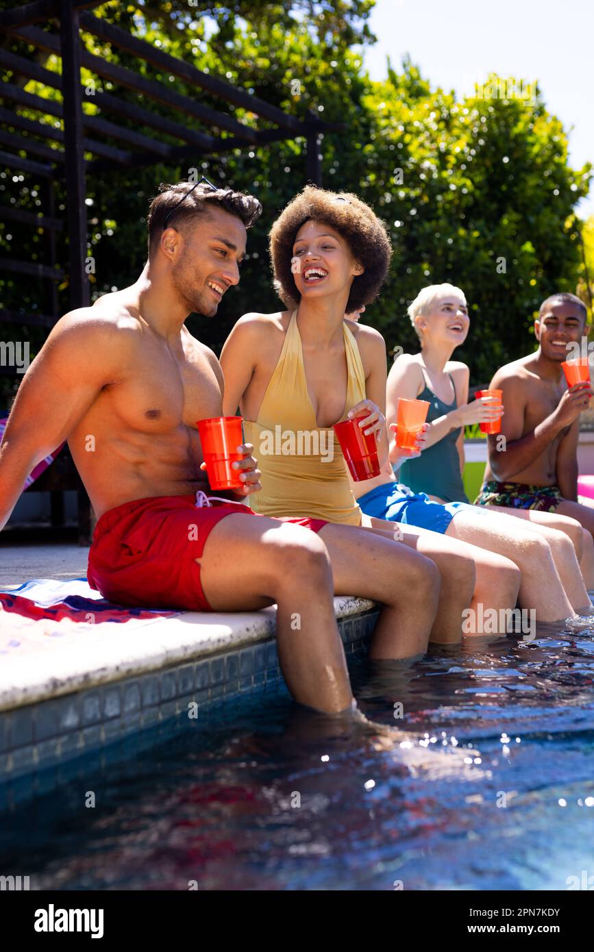 Fröhliche, vielfältige Gruppe von Freunden, die eine Poolparty veranstalteten und Plastikbecher im Garten hielten Stockfoto