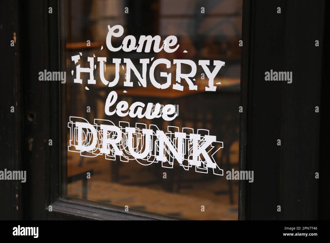 Schild mit der Aufschrift „Komm hungrig und lass dich betrunken“ im Fenster des Restaurants Stockfoto