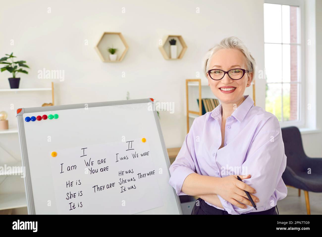 Eine glückliche, lächelnde Englischlehrerin, die im Klassenzimmer am Whiteboard steht Stockfoto