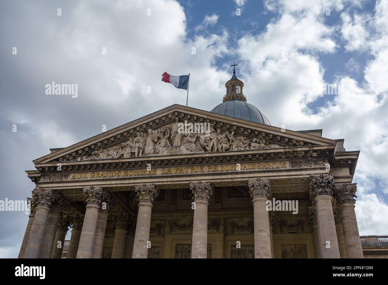 Pantheon in Paris, Frankreich. Der obere Teil und die französische Flagge vor dem wolkigen blauen Himmel. Stockfoto