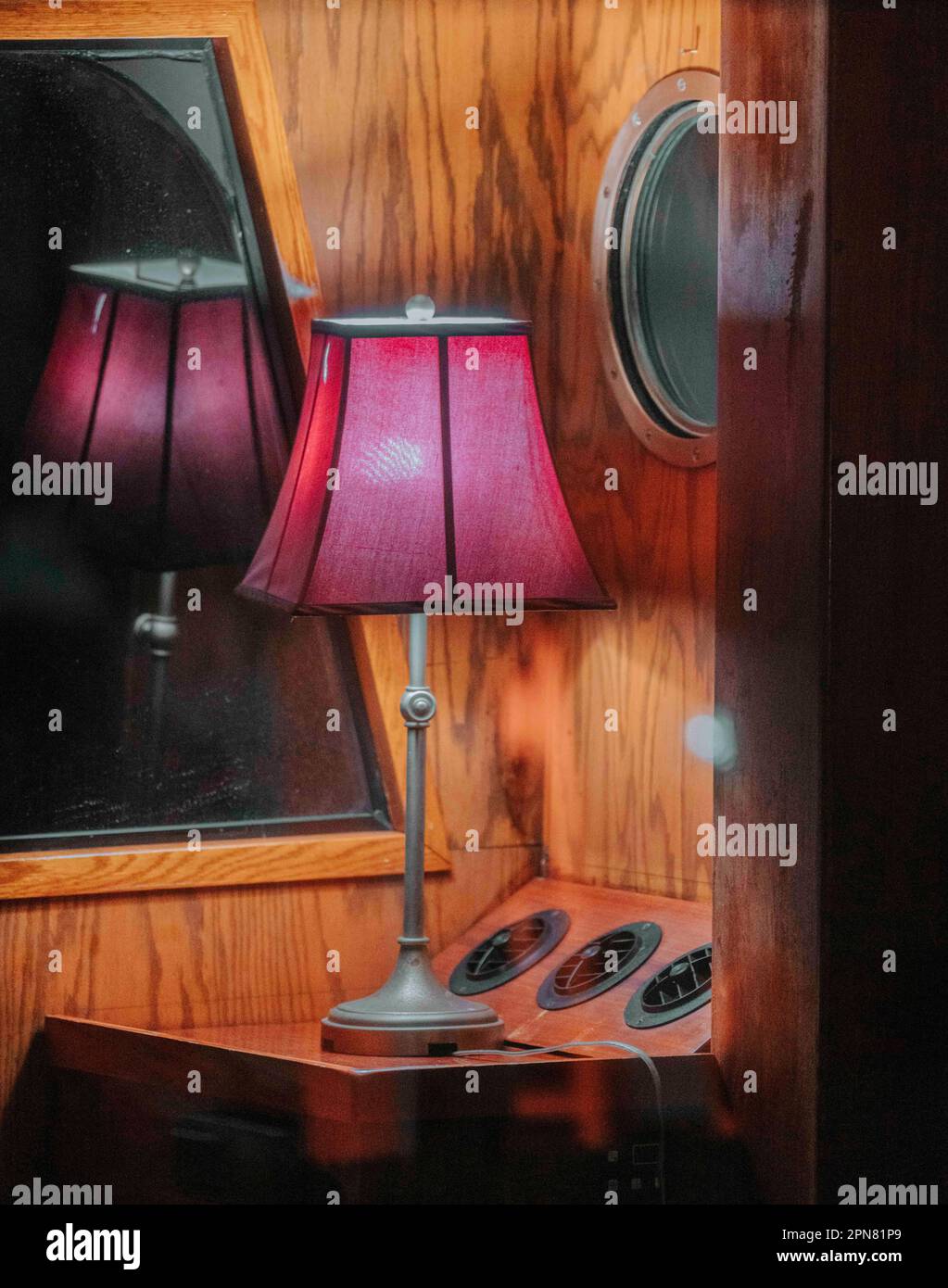Eine rustikal aussehende Lampe mit freiliegender Lampe befindet sich auf einem Holztisch unter einem großen Spiegel Stockfoto