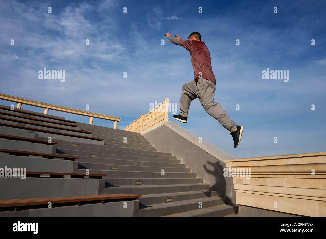 Sportler, der Parkour-Tricks im städtischen Raum vorführt. Parkoursportler, der hoch über die Treppe springt, draußen vor blauem Himmel. Extremsport, freier Außenbereich Stockfoto
