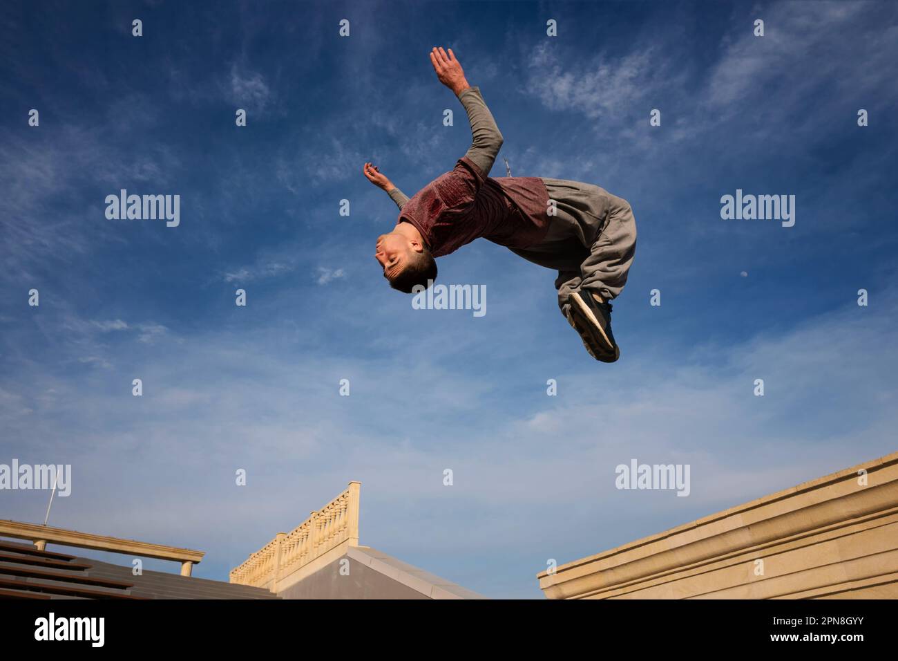 Ein Mann, der einen Salto gegen den blauen Himmel macht. Parkour-Sportler-Training in Sportkleidung in der Stadt. Free Runner Jumping haben ein Workout. Aktiver Lifestyle. Stockfoto