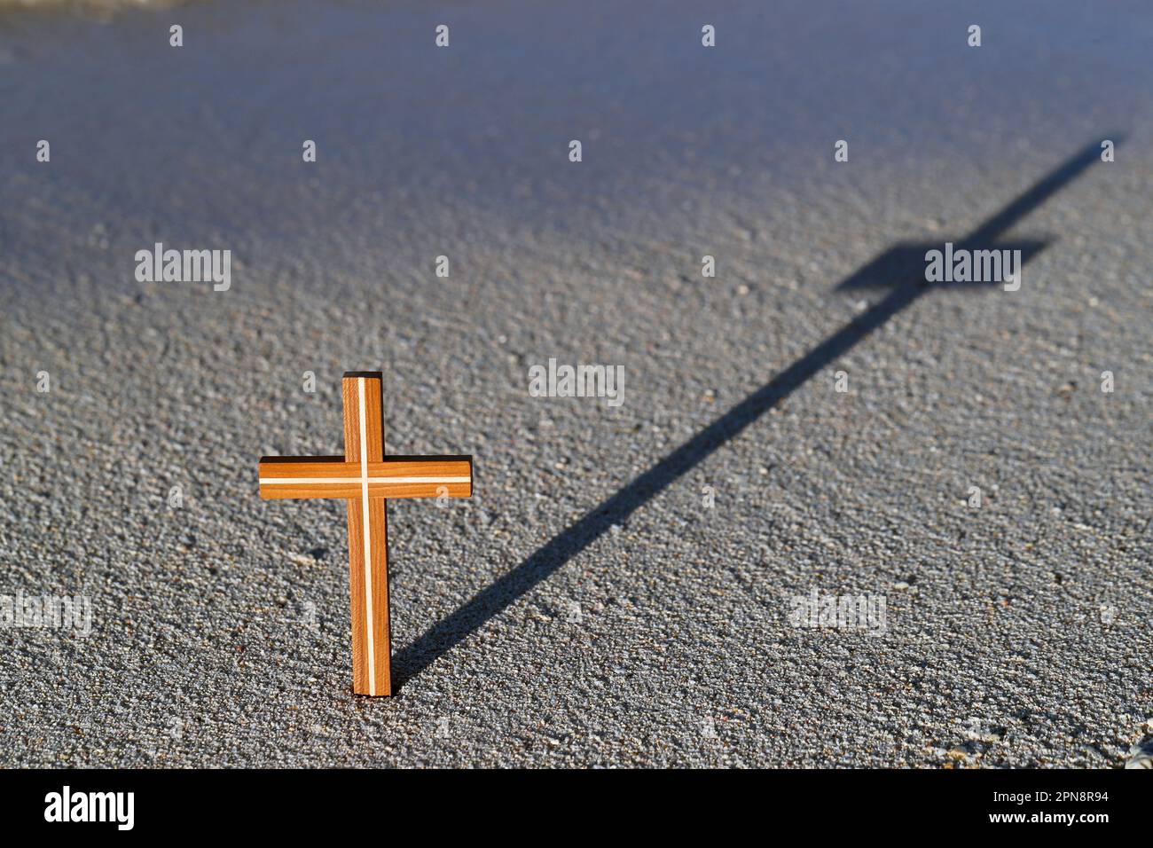 Ein hölzernes Kreuz im Sand mit Schatten. Konzept für Religion, Glauben und Spiritualität. Stockfoto