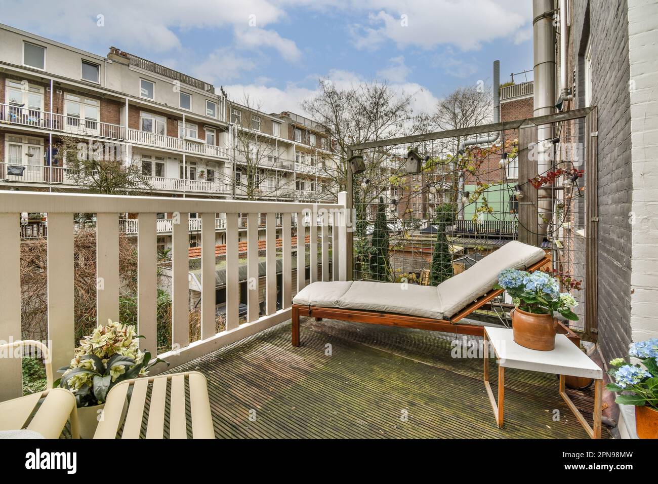 Ein Außenbereich mit Möbeln und Blumen auf dem Balkon, vor einigen weiß gestrichenen Apartmentgebäuden Stockfoto