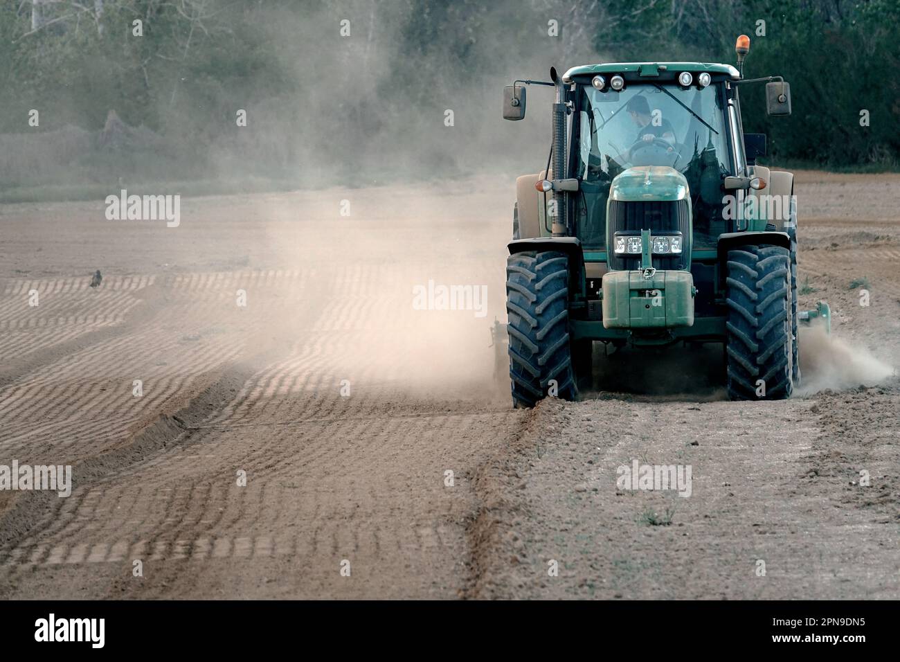 Der Traktor pflutet ein Feld, das von dem Staub trockener Erde nach langer Trockenheit umhüllt ist. Pianezza, Italien - April 2023 Stockfoto