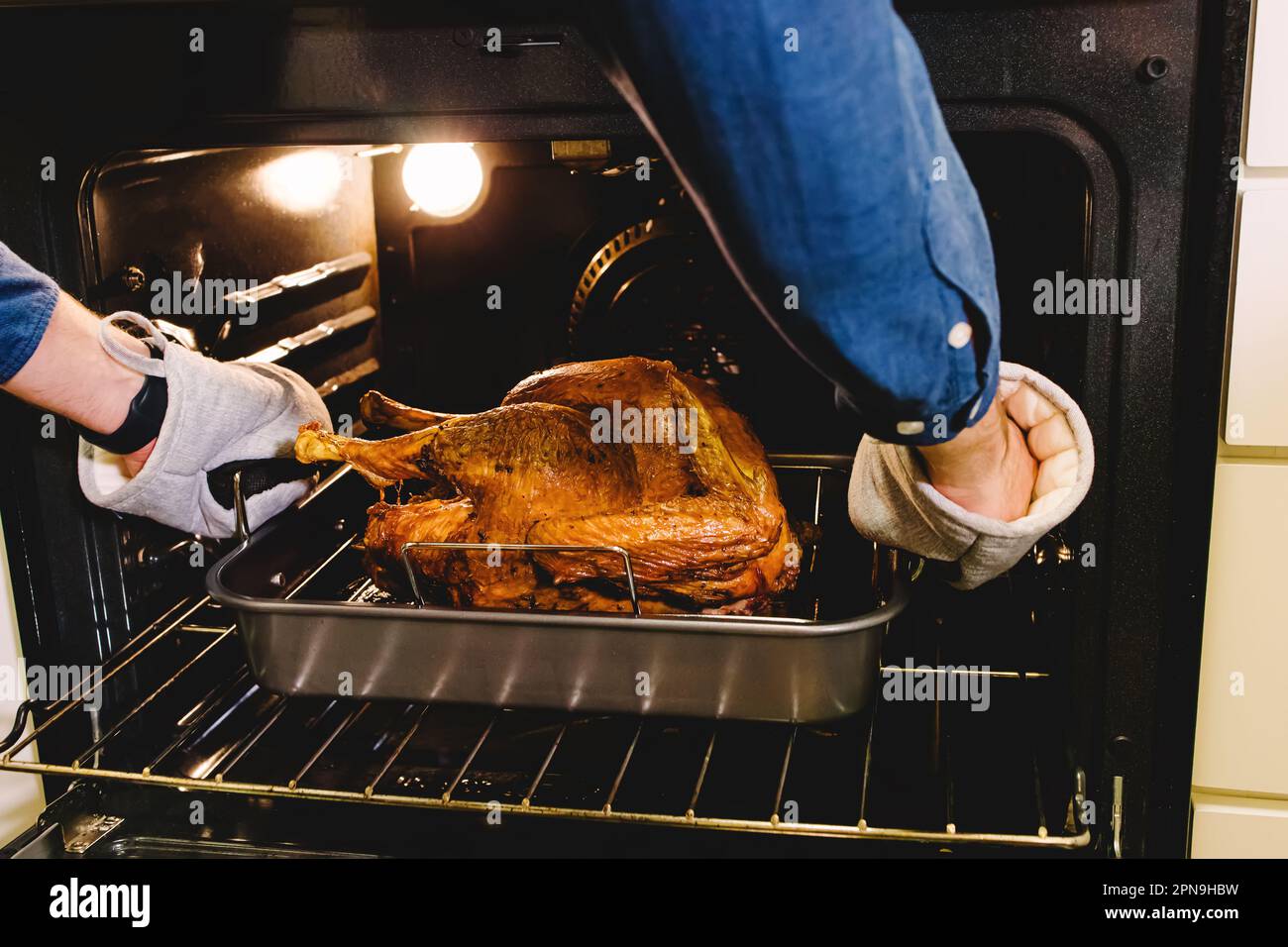 Ein unbekannter Mann, der knusprigen truthahn aus dem Ofen holt, Thanksgiving-Essenszubereitung Stockfoto