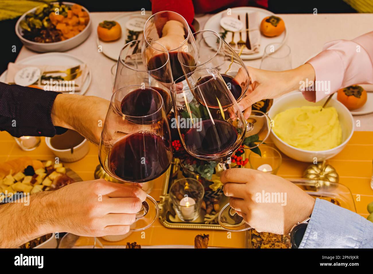 Nicht wiedererkennbare Leute, die mit einem Glas voller Rotwein am Thanksgiving-Esstisch herumklimperten. Feiern, versammeln, Friendsgiving Stockfoto