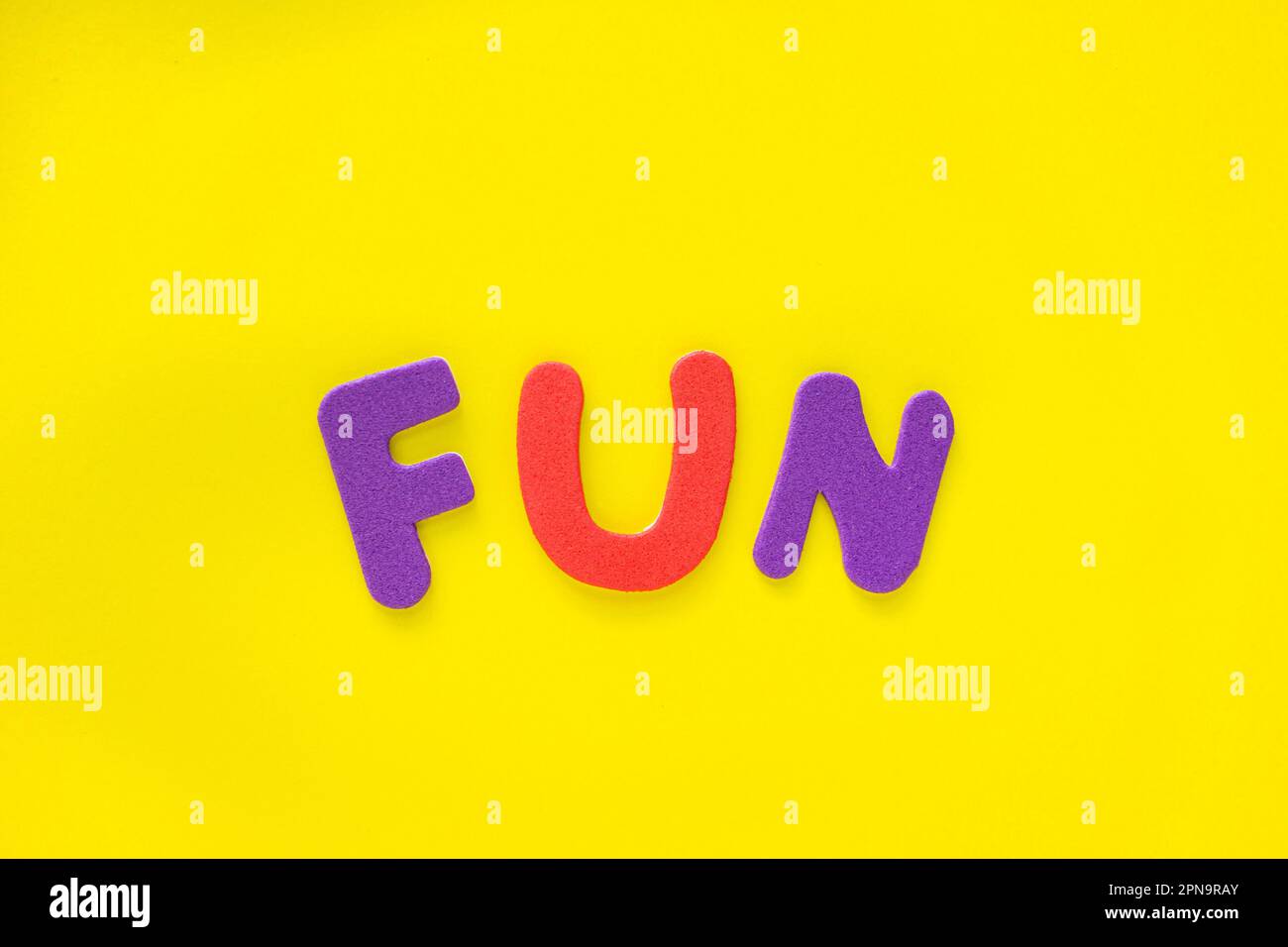 Farbiges Wort mit TEXTSPASS auf gelbem Hintergrund mit Kopierbereich. Farbige alphabetische Wörter bilden das Wort Spaß. Stockfoto