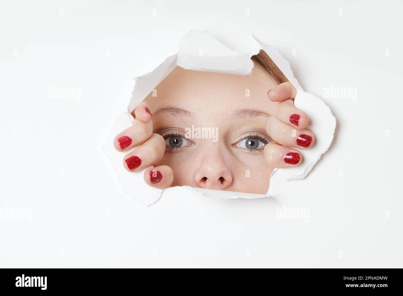 Junge Frau spähend durch das Loch in der Wand Stockfoto