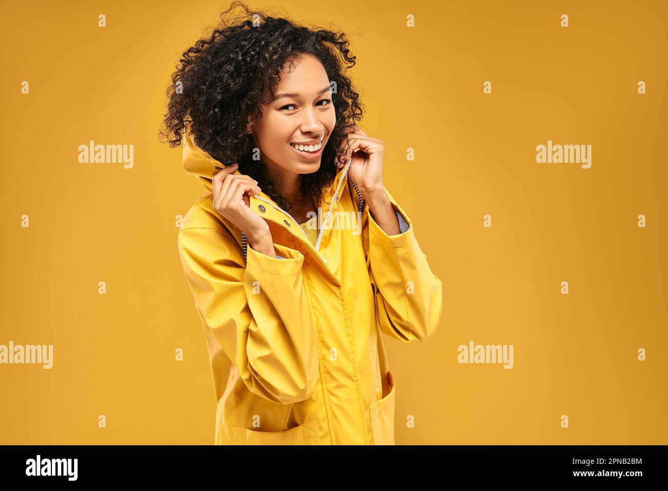 Eine glückliche afroamerikanische Frau trägt einen gelben Regenmantel mit Kapuze für regnerisches Wetter Stockfoto
