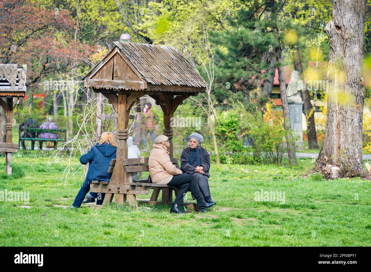 Bukarest, Rumänien - 2023. April: Gruppe von Seniorinnen, die auf Bänken im Park sitzen und sich unterhalten. Landschaft im King Mihai I Park ( He Stockfoto