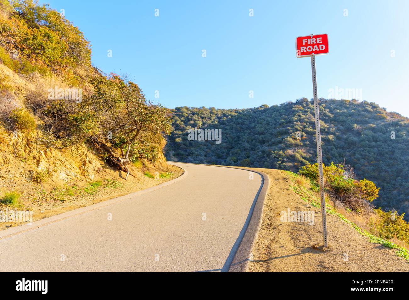 Feuerschutzschild am Straßenrand vor einer scharfen Kurve mit einem atemberaubenden blauen Himmel und dem üppigen kalifornischen Wald im Hintergrund. Stockfoto