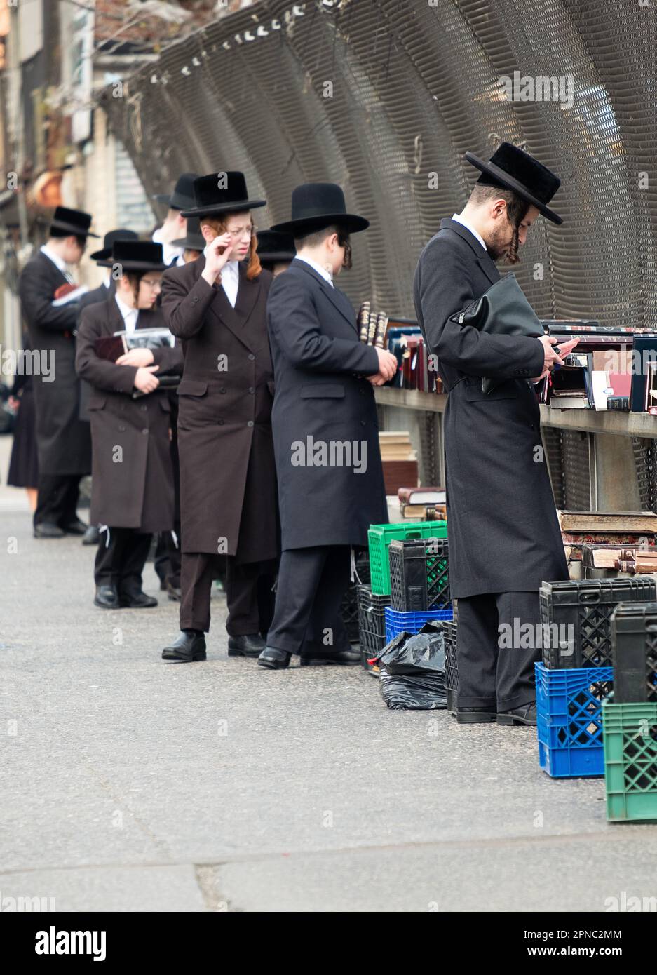 Chassidische jüdische Männer unterschiedlichen Alters versenden religiöse Bücher an einem Stand auf der Straße mit Blick auf die BQE in Williamsburg, Brooklyn, New York. Stockfoto