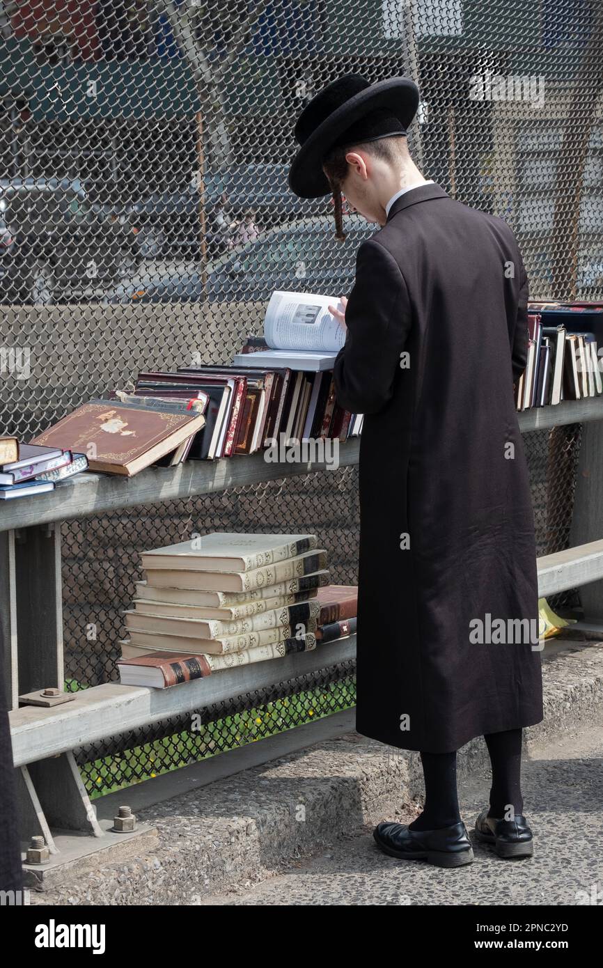 Ein junger jüdischer Mann, der ganz schwarz trägt, einschließlich hoher schwarzer Strümpfe, kauft Bücher bei einem Pop-up-Sale im Freien. In Brooklyn, New York. Stockfoto