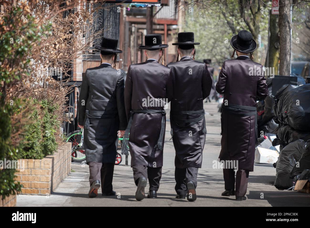 4 anonyme, fast identisch gekleidete chassidische jüdische Männer gehen eine Straße entlang in Brooklyn, New York. Stockfoto