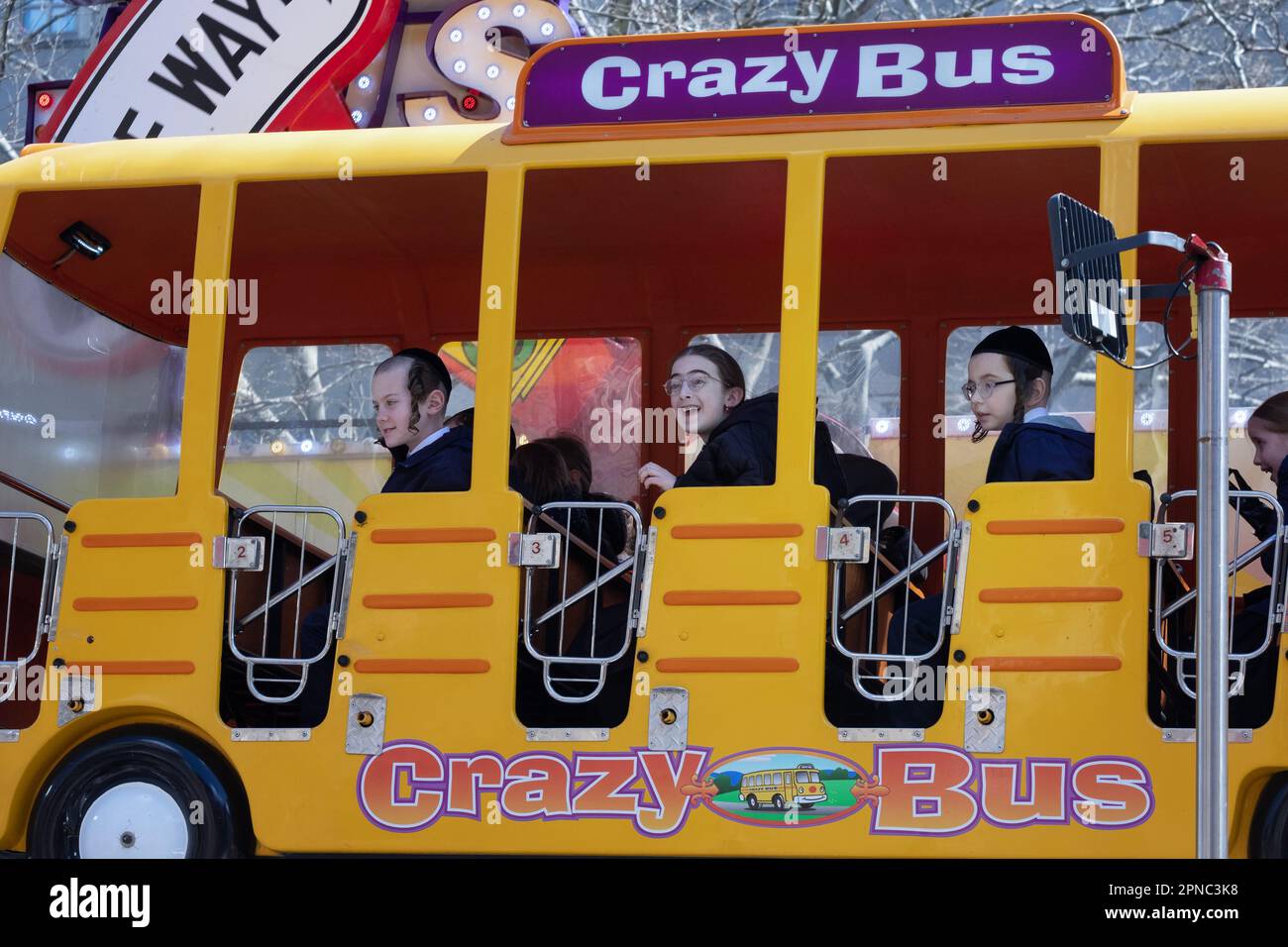 Während des Passover, wenn es zum Spaß verpflichtet ist, fahren chasidische Kinder mit dem Crazy Bus in einem temporären Outdoor-Vergnügungspark in Williamsburg, Brooklyn, N. Stockfoto