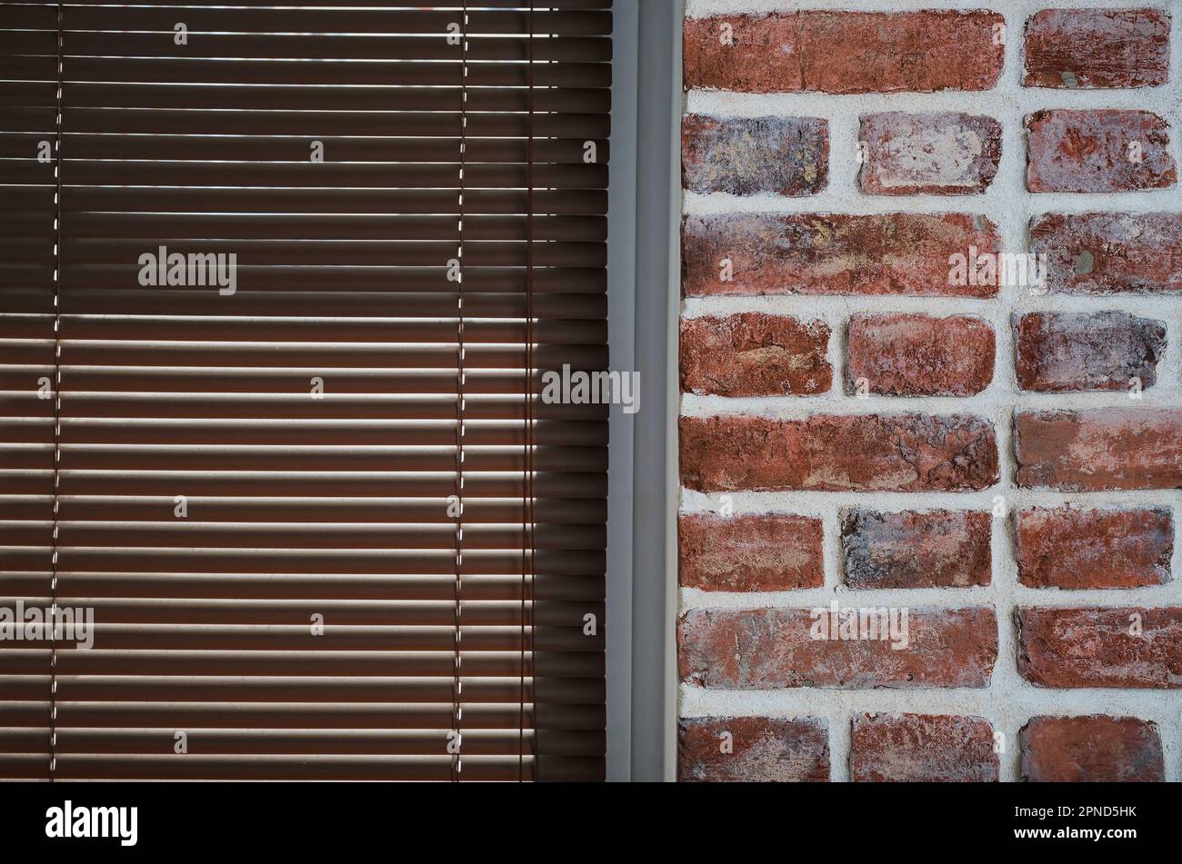 Fenster mit braunen Jalousien und einer Backsteinwand aus alten Ziegeln, Dachboden-Innenraum, industrielle Inneneinrichtung als Hintergrund, Nahaufnahme Stockfoto