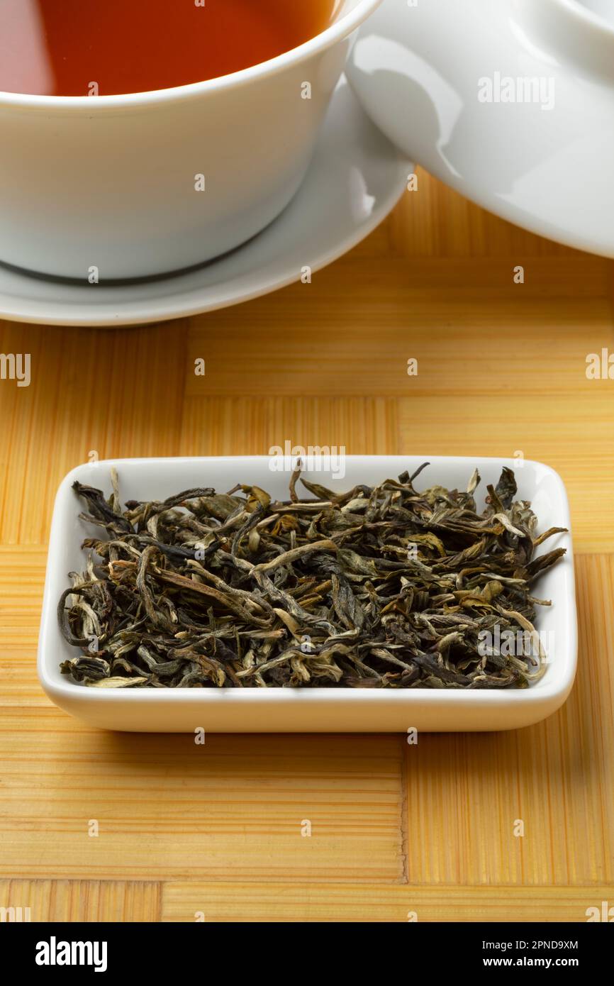 Getrocknete Teeblätter mit weißem Affentee, Bai Mao Hou, auf einer Schüssel, dicht vor einer Tasse Tee Stockfoto
