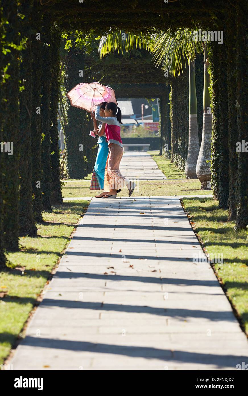 Zwei Mädchen mit einem Regenschirm spazieren durch das Rangoon Memorial, das sich im Zentrum des Taukkyan war Cemetery (Htauk Kyant war) in Mingaladon, Myanmar befindet. Stockfoto