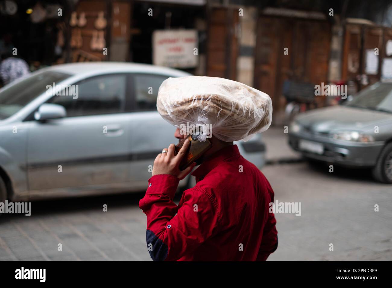 Ein Mann mit Handy auf der Straße trägt arabisches Brot auf dem Kopf, Stockfoto