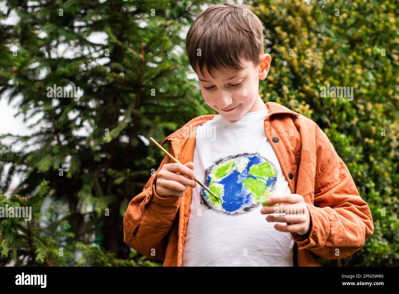 Nachhaltiges Lifestyle-Konzept. Schuljunge, der Erdkugel auf T-Shirt malt. Grüne Energie, ESG, erneuerbare Ressourcen, Umweltschutz, Schutz des Planeten Stockfoto