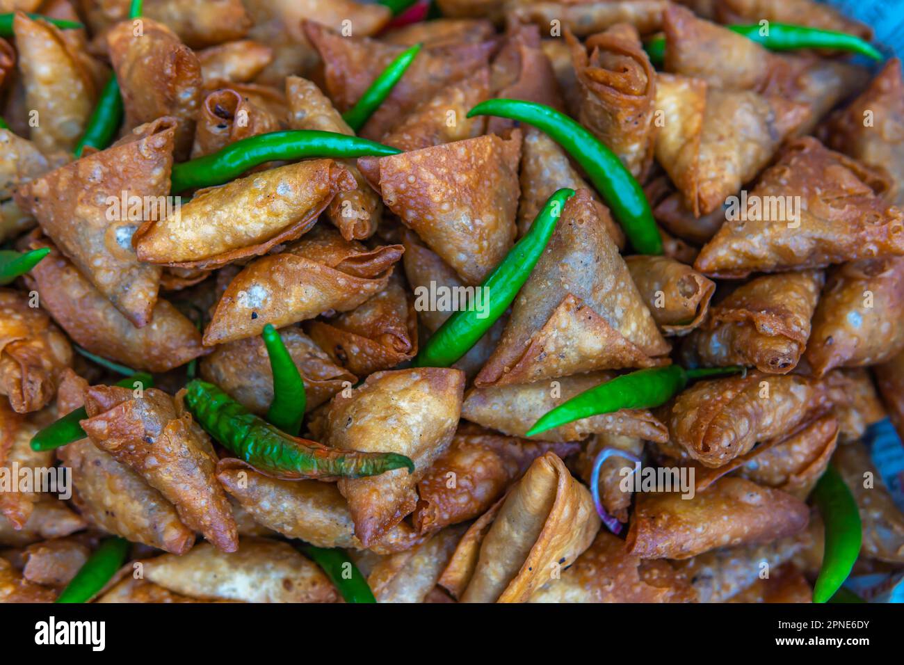 Frisch zubereitete Samosa zum Servieren mit einer frischen grünen Chilischote. Stockfoto