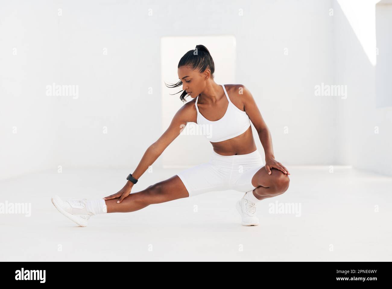 Eine Frau in weißer Fitnesskleidung wärmt ihren Körper und ihre Beine auf. Eine Frau, die Stretching-Übungen in einem weißen Outdoor-Studio macht. Stockfoto