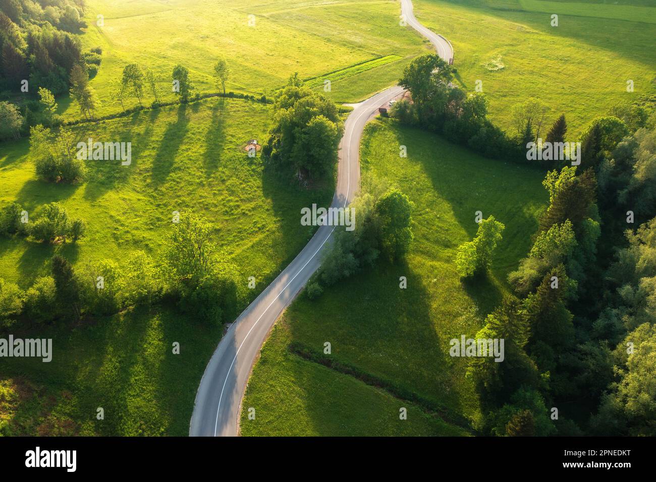 Luftaufnahme der Straße auf grünen Wiesen und Hügeln bei Sonnenuntergang Stockfoto