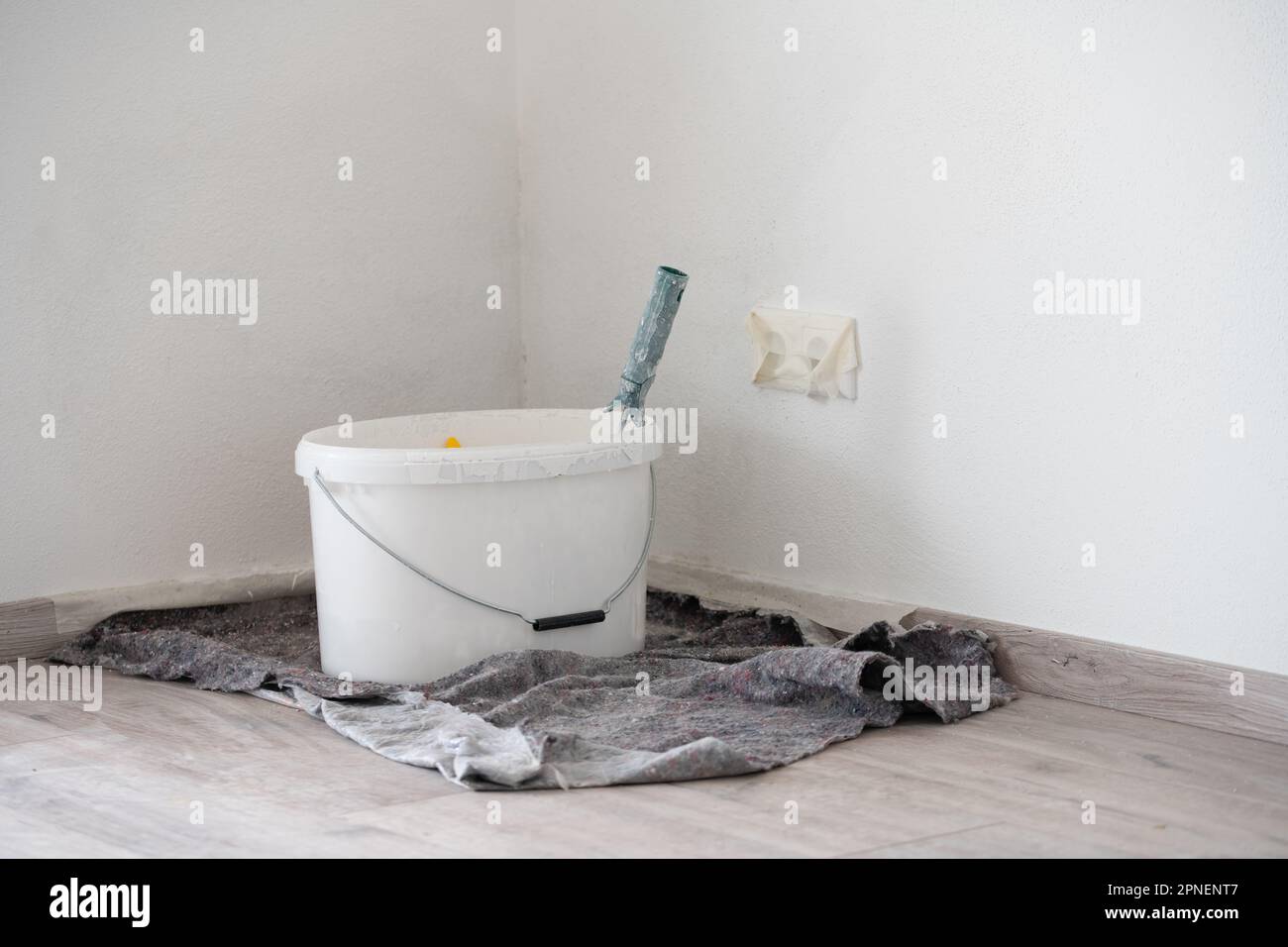 Ein Eimer mit weißer Farbe befindet sich in der Ecke eines Raumes. Die Buchsen sind mit Klebeband versehen. Stockfoto