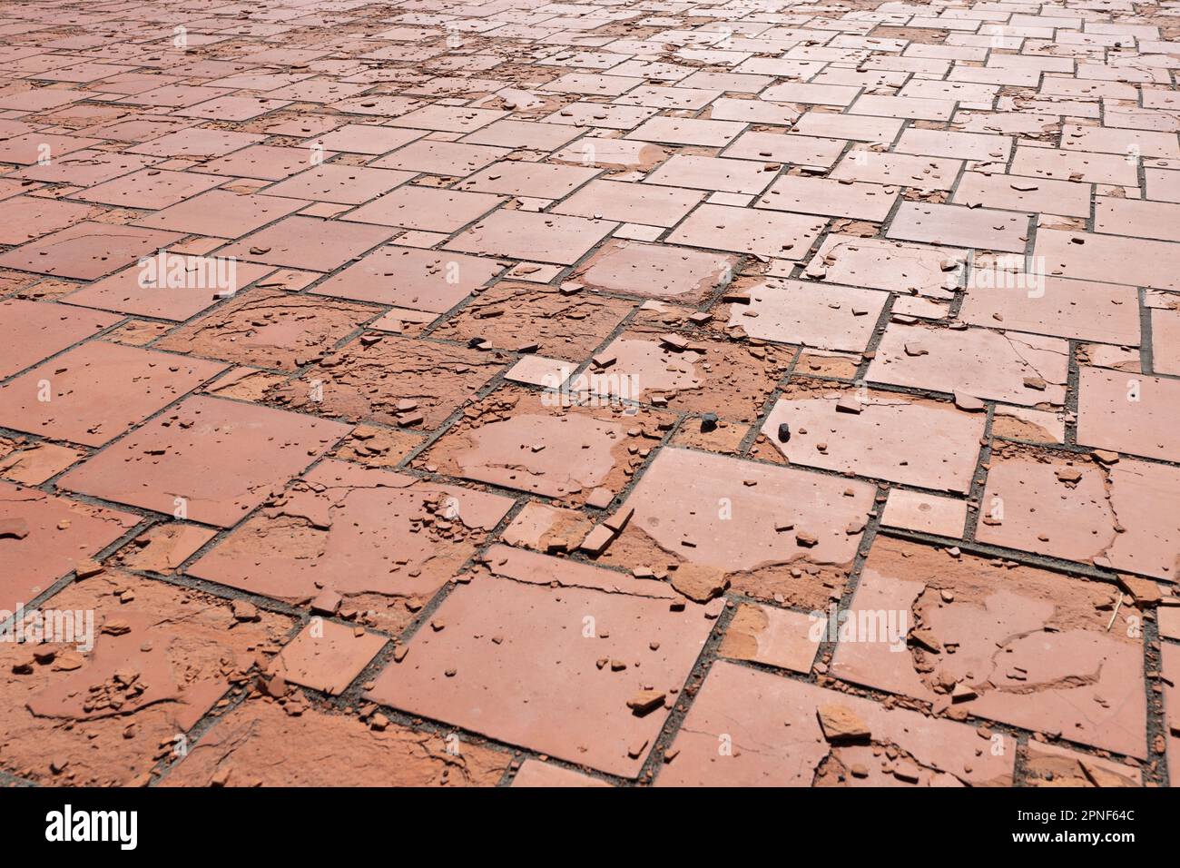 Rote quadratische Bodenfliesen, die durch Witterungseinflüsse oder Materialfehler beschädigt wurden. Die Oberfläche bröckelt und die Platten zerfallen. Stockfoto