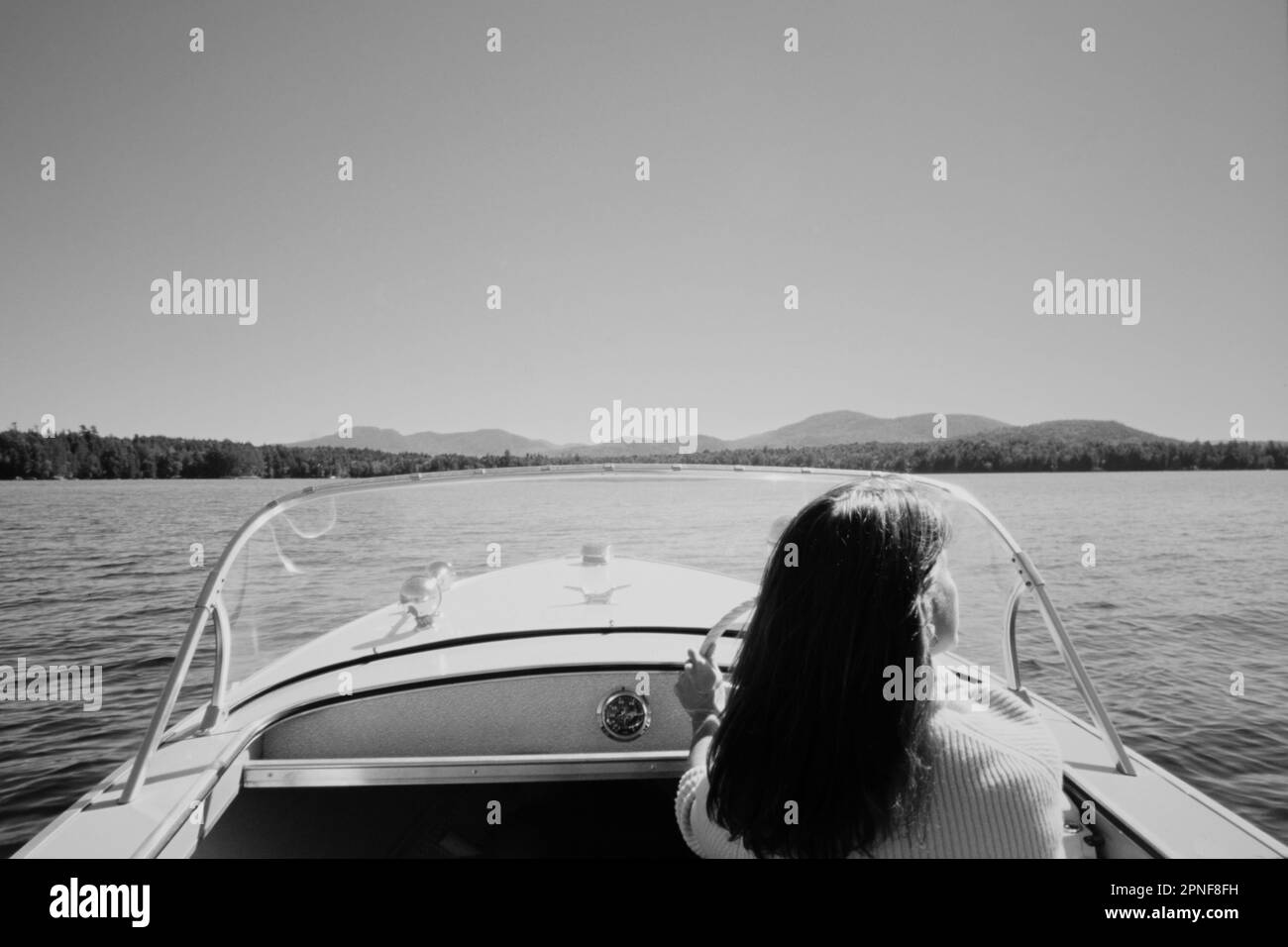 USA, New York, Santa Clara, Rückansicht einer Frau, die auf dem Upper Saranac Lake Motorboot fährt, schwarz-weiß Stockfoto