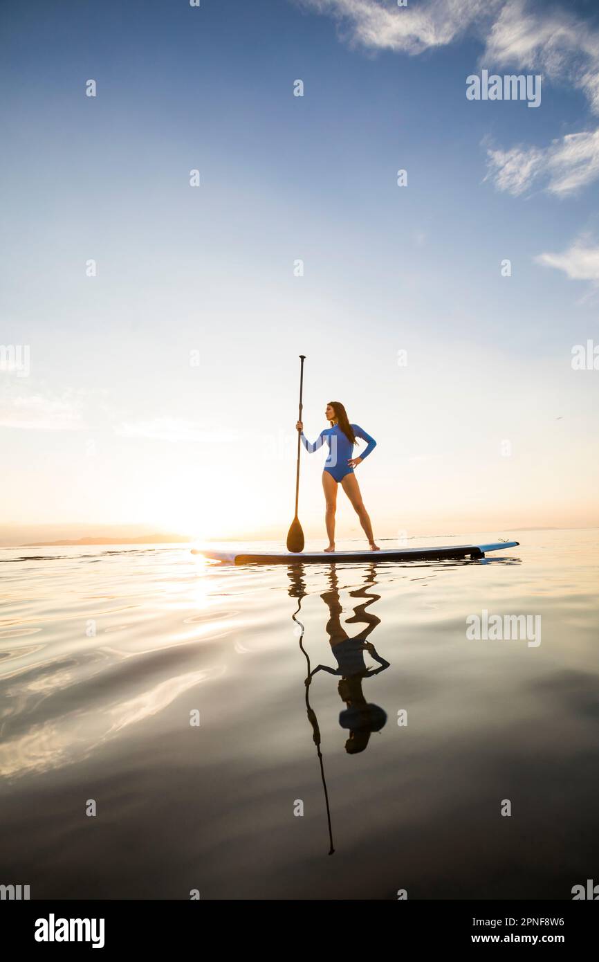 Eine Frau, die bei Sonnenuntergang auf dem Paddleboard steht Stockfoto