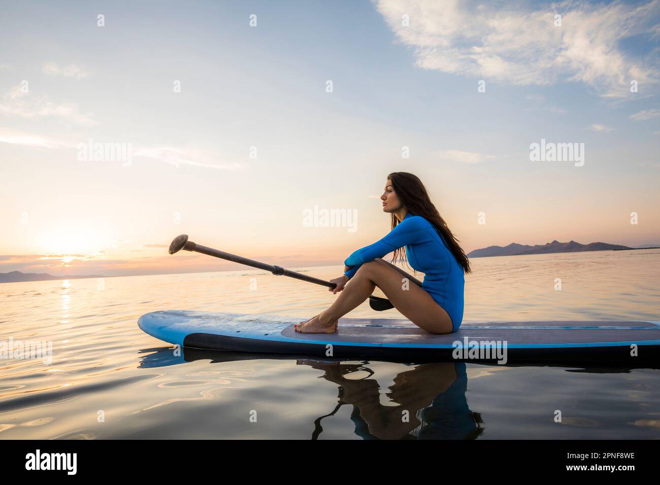 Eine Frau, die bei Sonnenuntergang auf dem Paddleboard sitzt Stockfoto