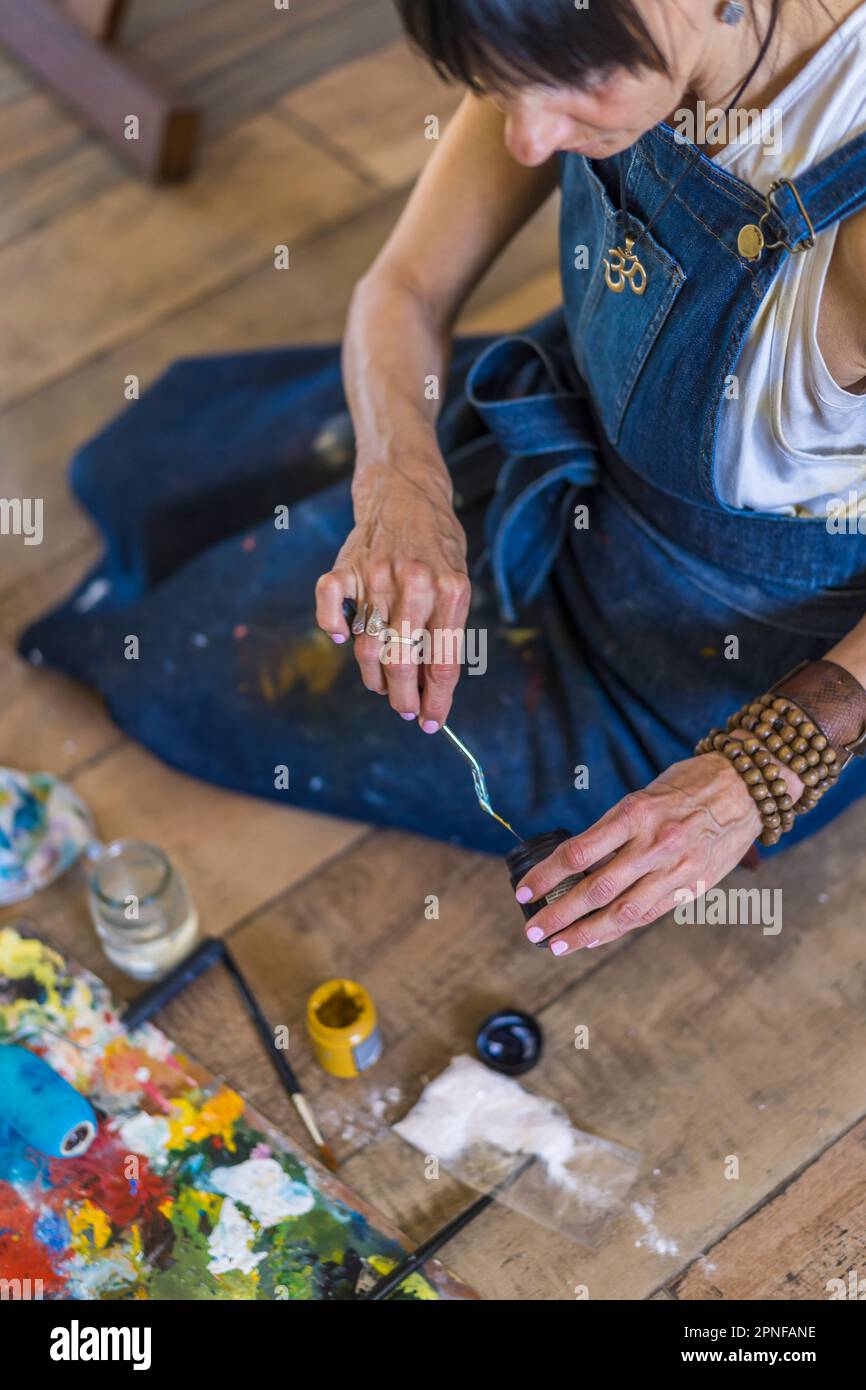 Künstlerin malt auf einer Leinwand ein blaues abstraktes Gemälde. Kreative Frau, die in ihrem Kunstatelier auf dem Boden arbeitet. Stockfoto