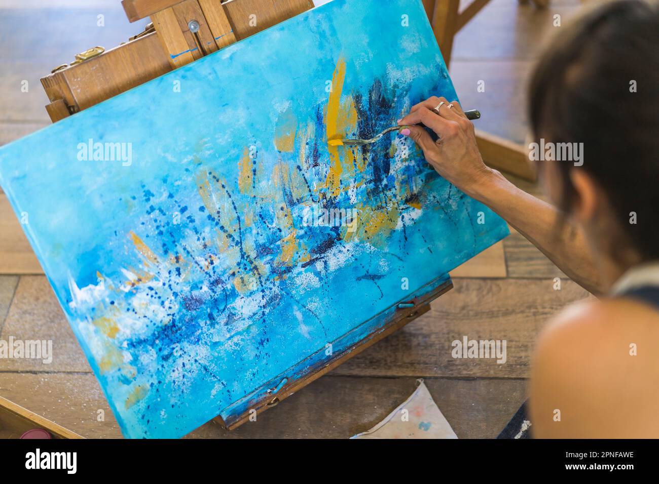 Nahaufnahme einer Frau, die auf einer Leinwand malt, ein blaues abstraktes Gemälde. Stockfoto