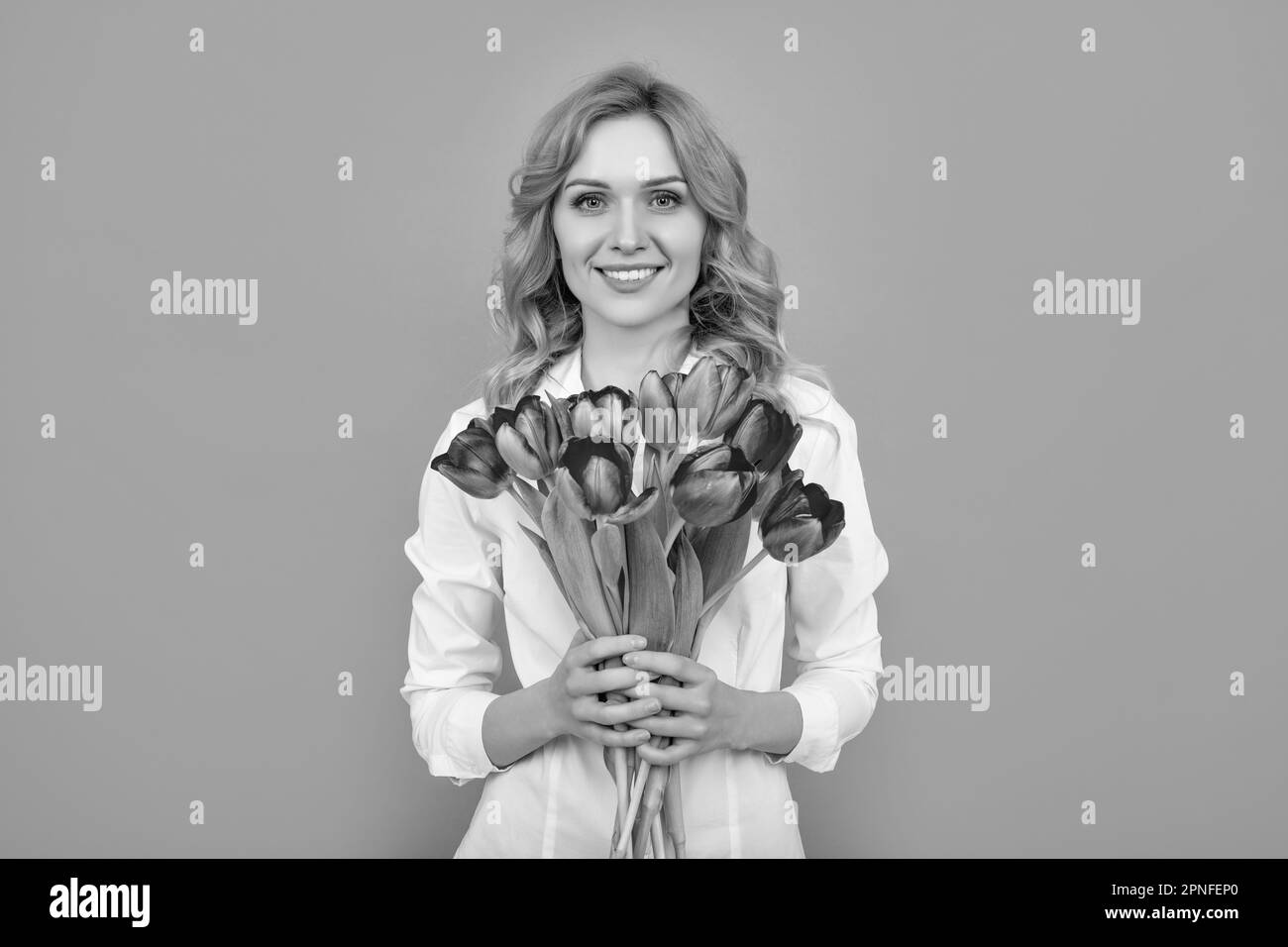 Lächelnde blonde Frau mit Frühlingsblumen auf grauem Hintergrund Stockfoto