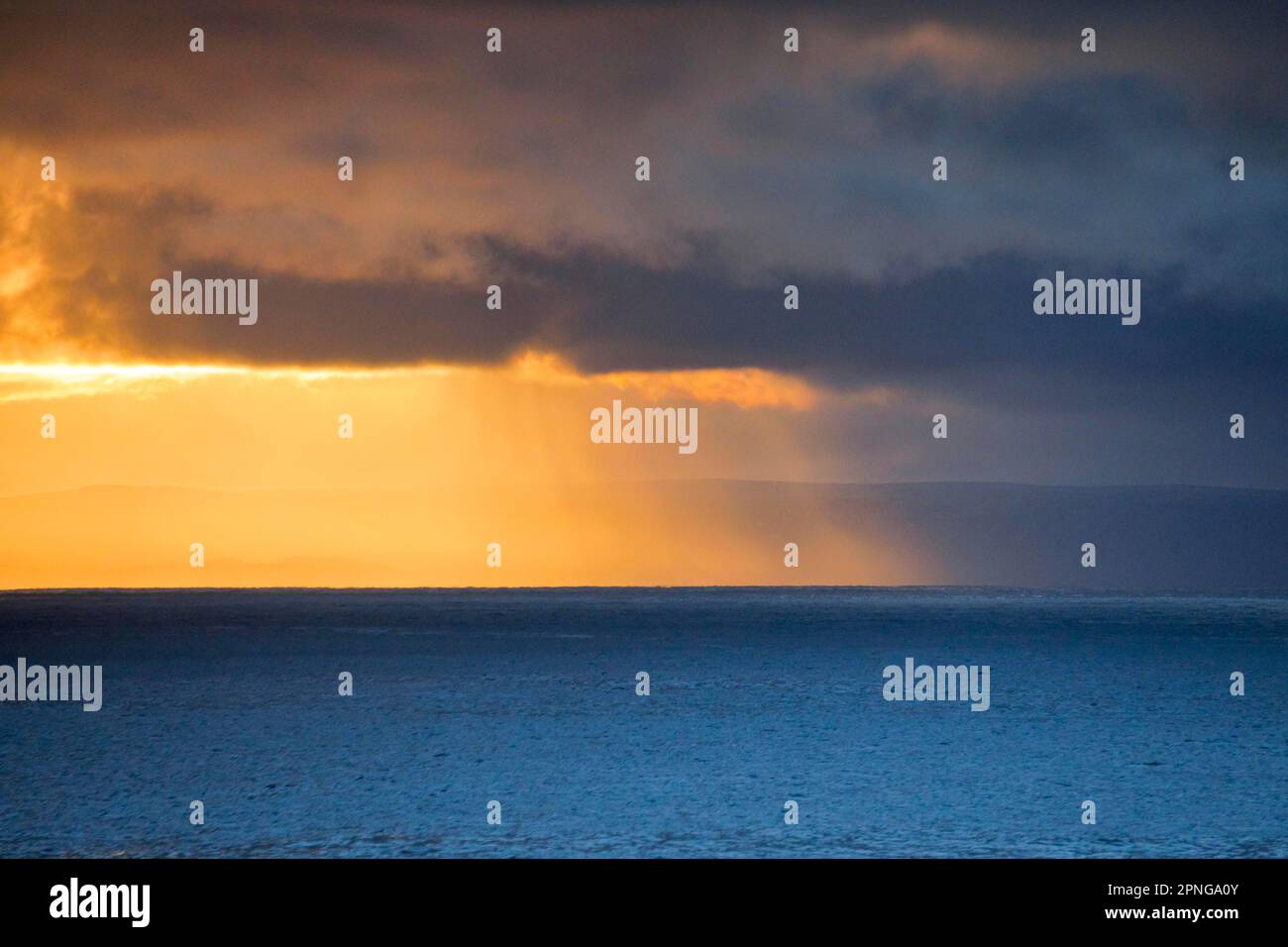 Die Abendsonne bricht durch tief liegende Regenwolken über den Sommerinseln und dem offenen Wasser des blauen Atlantiks an der Westküste Schottlands Stockfoto