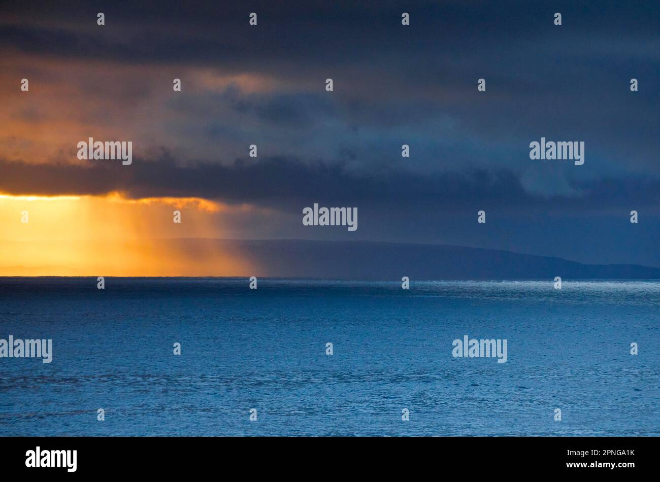 Die Abendsonne bricht durch tief liegende Regenwolken über den Sommerinseln und dem offenen Wasser des blauen Atlantiks an der Westküste Schottlands Stockfoto