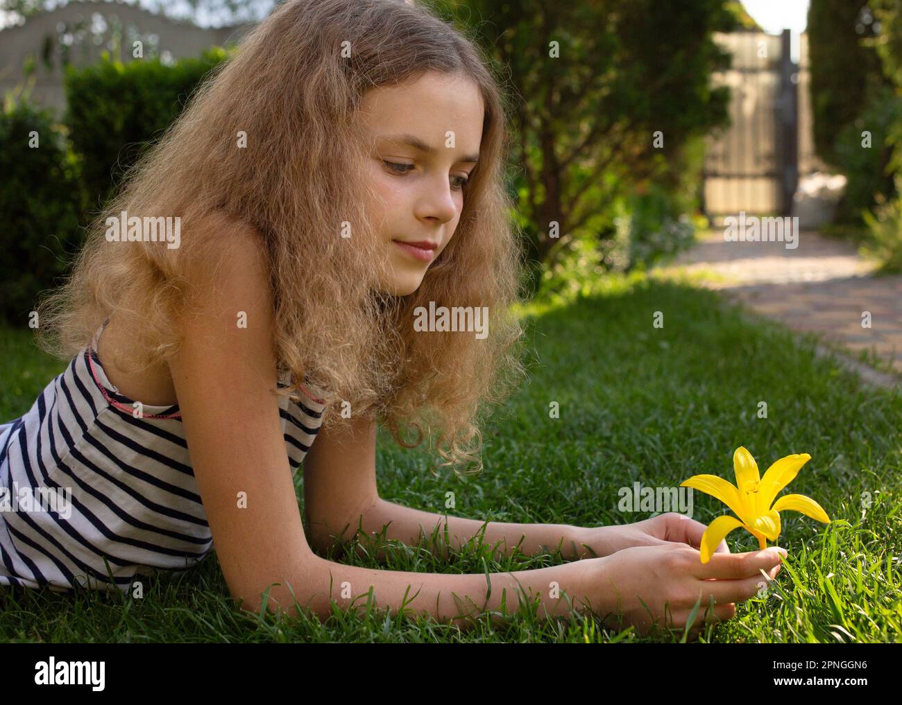 Porträt eines wunderschönen, 12 Jahre alten Mädchens, das am sonnigen Tag auf Gras lag, Tagträumen, Blumen in den Händen sah Stockfoto