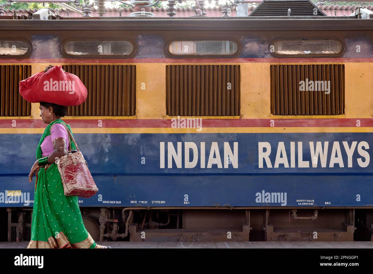 Eine indische Frau, die ein Bündel Kleider auf dem Kopf trägt, fährt an einer Eisenbahnwaggon der indischen Eisenbahn vorbei: Chhatrapati Shivaji Maharaj Terminus, Mumbai, Indien Stockfoto