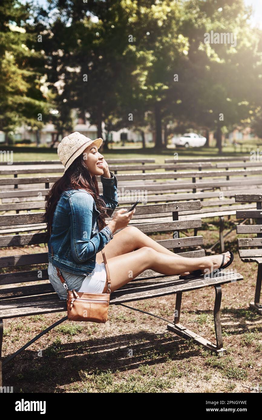 Sie sind nie ganz allein, wenn Sie mit Technologie arbeiten. Eine attraktive junge Frau, die ein Handy im Park benutzt. Stockfoto