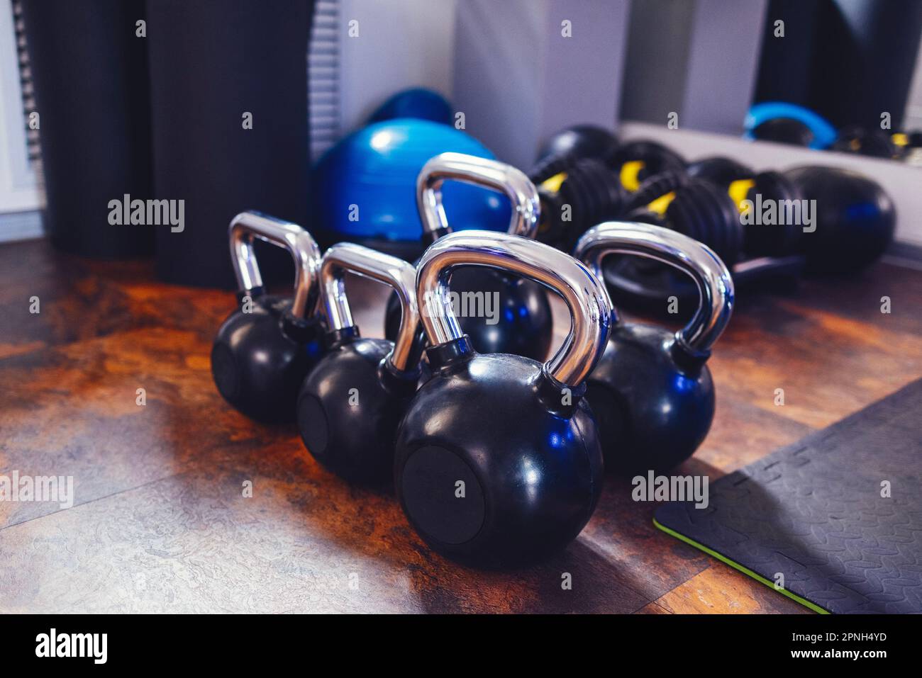 Fünf schwarze Kugelhanteln mit unterschiedlichen Gewichten. Sportgeräte im Fitnessraum. Verstellbare Kurzhanteln, Gymnastikhemisphäre, gewichteter Ball und Yogamatten Stockfoto