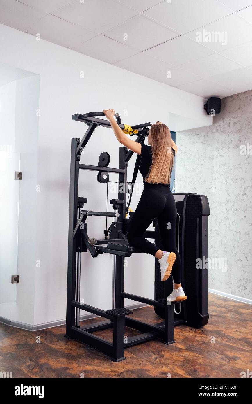 Fit Woman fährt im Sportsimulator an. Angespannte Sportlerinnen trainieren auf einem gravitron-Gerät im Fitnessstudio. Rückansicht einer Sportlerin, die sportliche Übungen macht Stockfoto