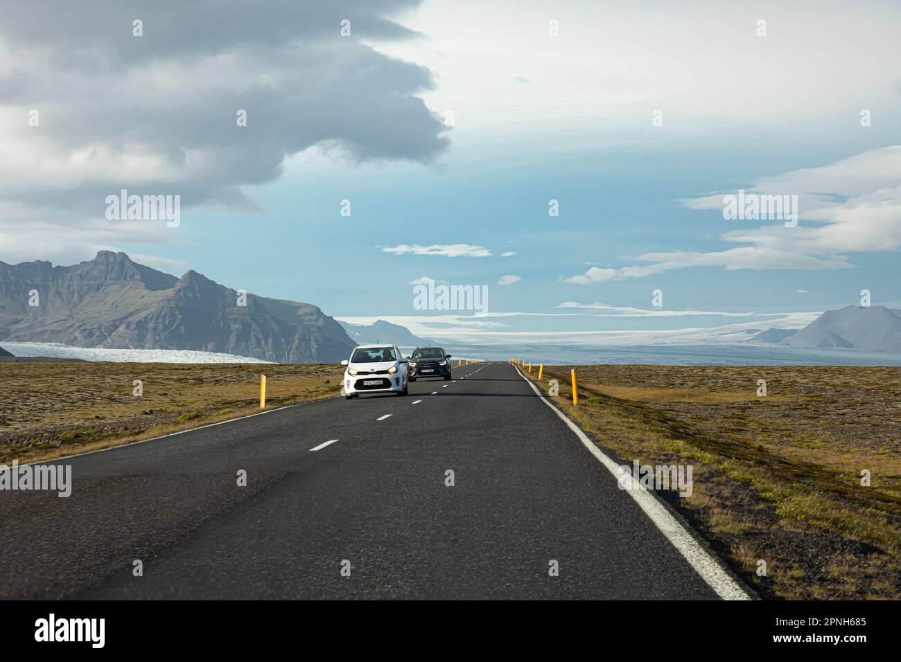 Island - August 2021: suv-Autos auf einer isländischen Straße mit wunderschöner grüner Landschaft, schneebedeckten Bergen und Vatnajokull-Gletscher im Hintergrund Stockfoto