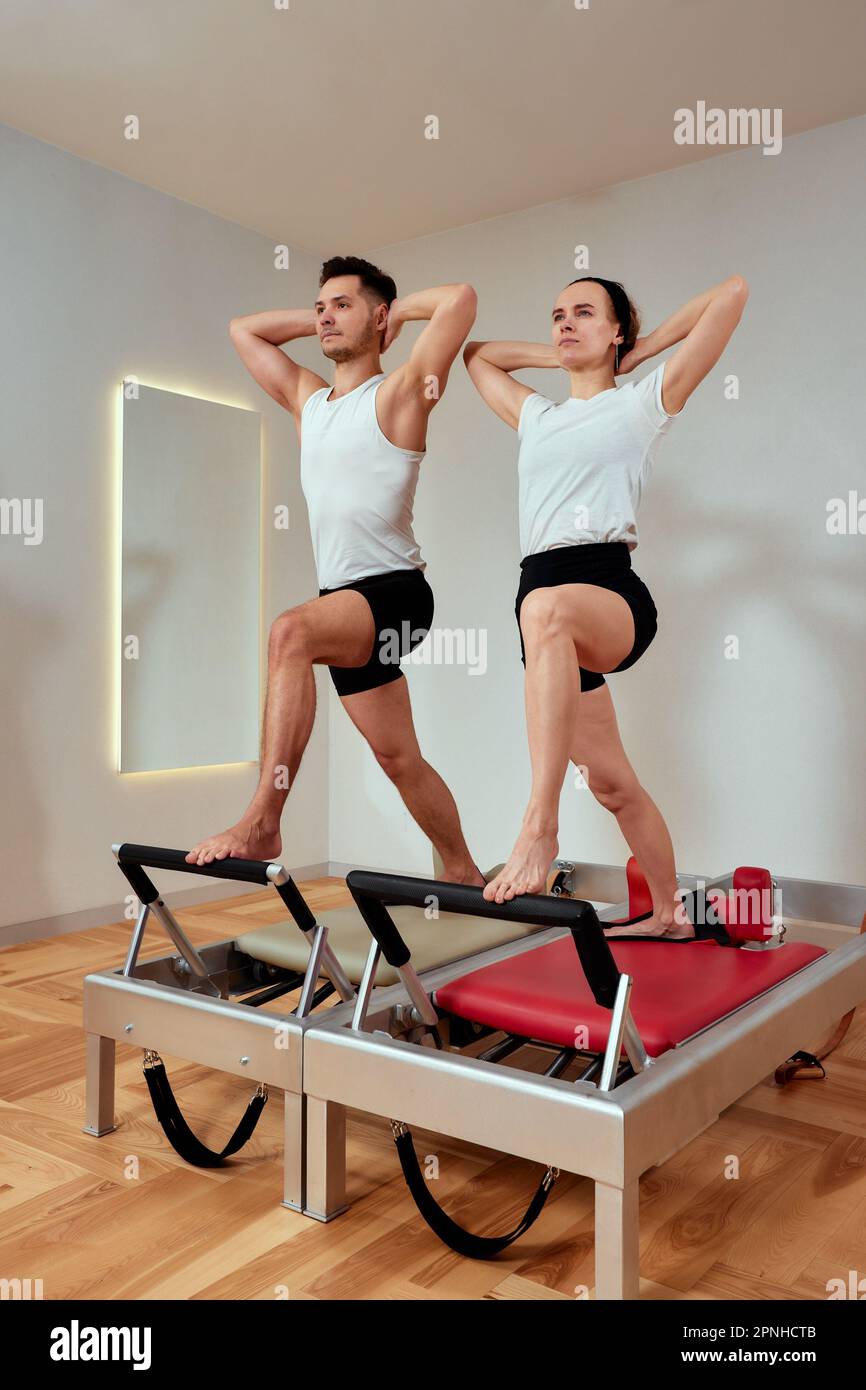 Ein Mann und eine Frau in einem Paar machen Pilates an Reformern, Mann und Frau der Vielfalt, paarweise Übungen an einem Reformer, um das Bewegungsapparat wiederherzustellen Stockfoto