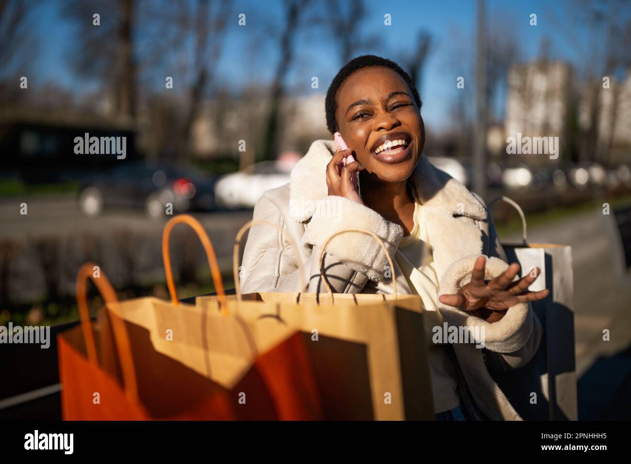 Außenporträt einer glücklichen schwarzen Frau. Sie sitzt nach dem Einkaufen auf der Bank auf der Straße. Stockfoto