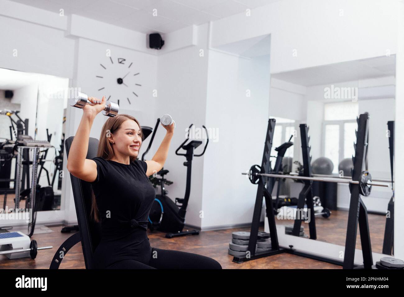 Eine sportliche junge blonde Frau in schwarzer Sportbekleidung presst auf einer geneigten Universalbank im Fitnessstudio oder Fitnessstudio die Kurzhantel. Pumpen der Muskeln von b Stockfoto