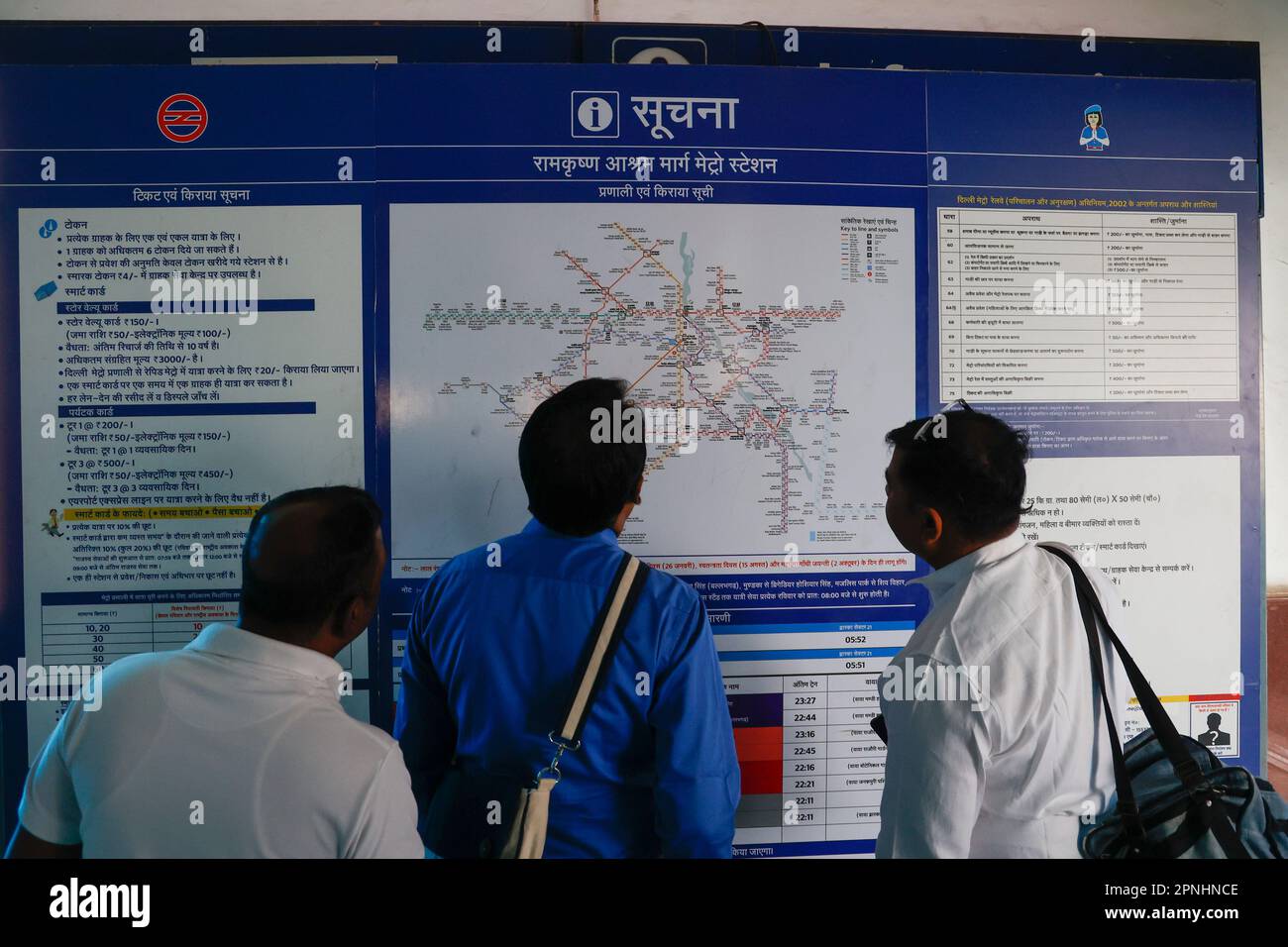 Drei Männer schauen auf die Karte der öffentlichen Verkehrsmittel an der Ramakrishna Ashram Marg Metro Station in Delhi, Indien Stockfoto