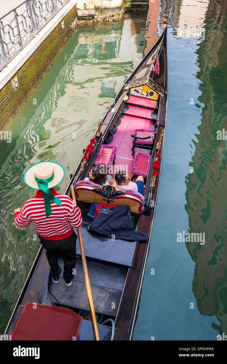 Gondoliere mit Hut im Gondelboot in einem Wasserkanal, Venedig, Venetien, Italien Stockfoto